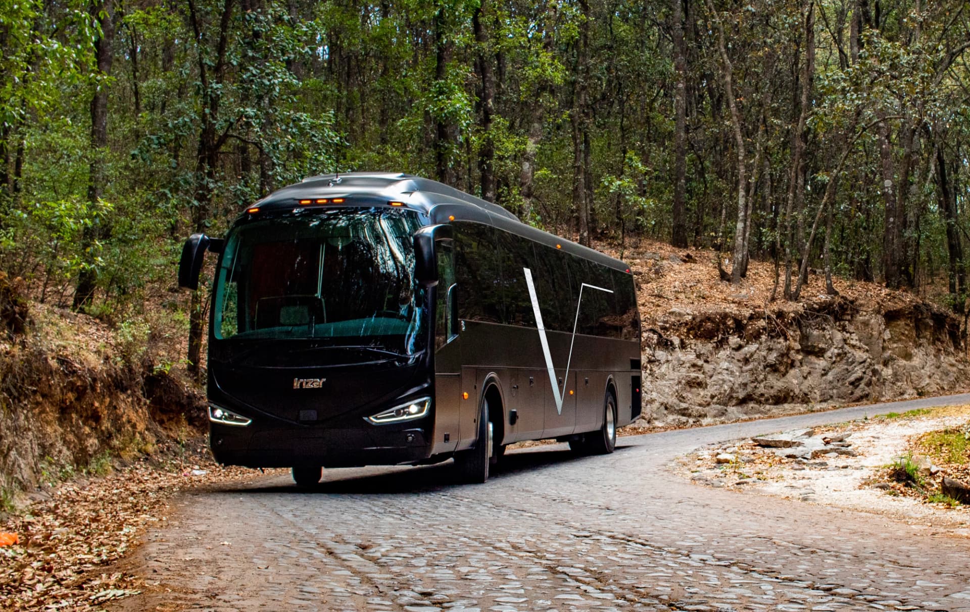Bus ejecutivo Irizar V transfers en camino empedrado entre el bosque